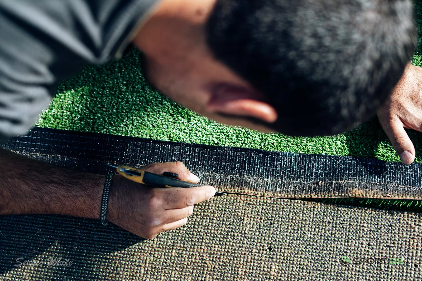 Installer trimming artificial turf during padel court installation