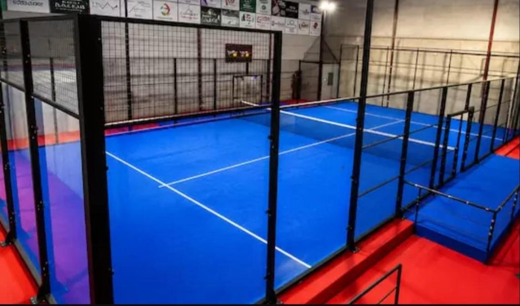 Indoor padel court installation in the UK: blue court with black steel structure and glass walls inside an existing building