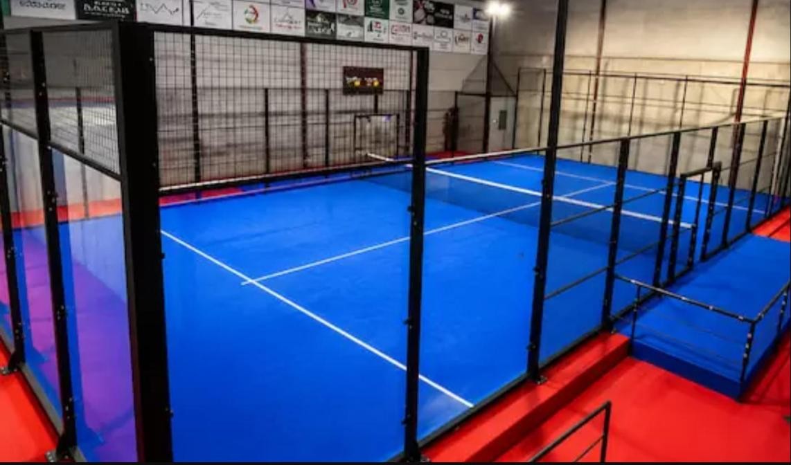 Indoor padel court installation in the UK: blue court with black steel structure and glass walls inside an existing building