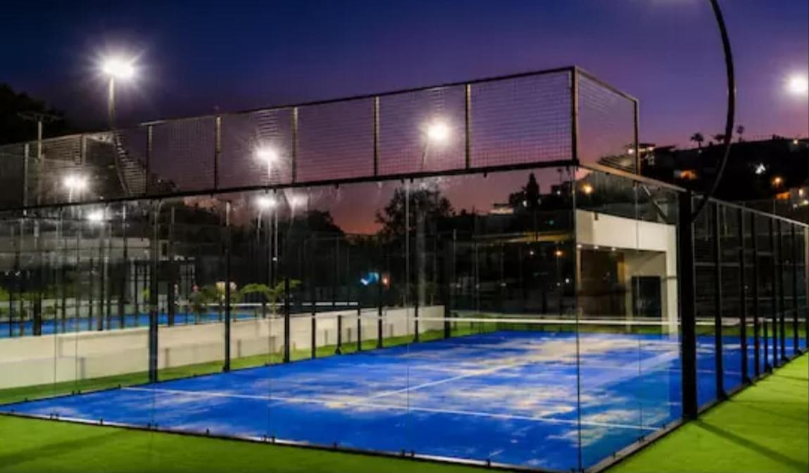 Padel court manufacturers: SportBS outdoor court with black steel structure, glass walls, blue turf and LED lighting at night